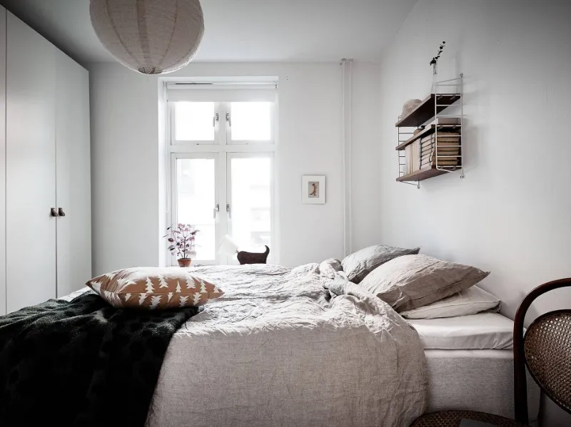 Scandinavian apartment hotel bedroom with upholstered bed, wardrobe and wall shelving